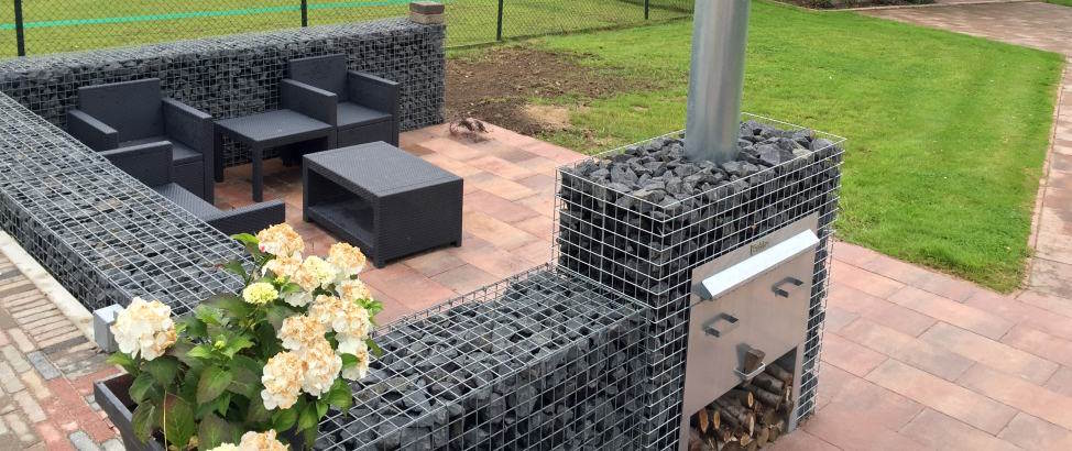 Ein großzügiger Außenbereich mit einem Gabionen-Gartenkamin umgeben von Sitzmöbeln sorgt für Gemütlichkeit und Wärme