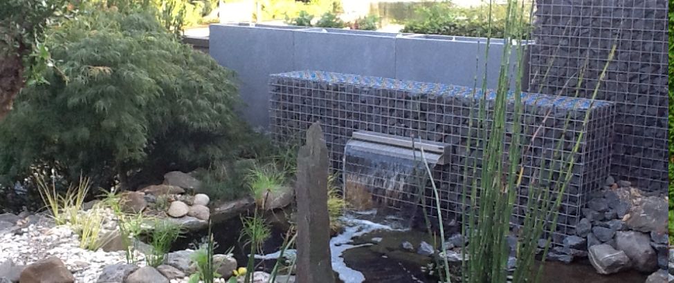 Gabionen-Wasserfall an einem Gartenteich mit Wasserpflanzen und Steinkörben