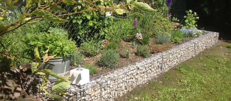 Klares und robustes Gartendesign mit dem Gabionen Hochbeet 100x80x60. Gabionen Hochbeet 100x80x60 auf einer Terrasse mit Pflanzen aufgestellt